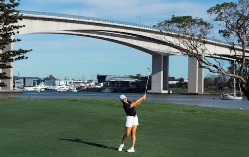 Woman playing golf near Gateway Bridge over Brisbane River.